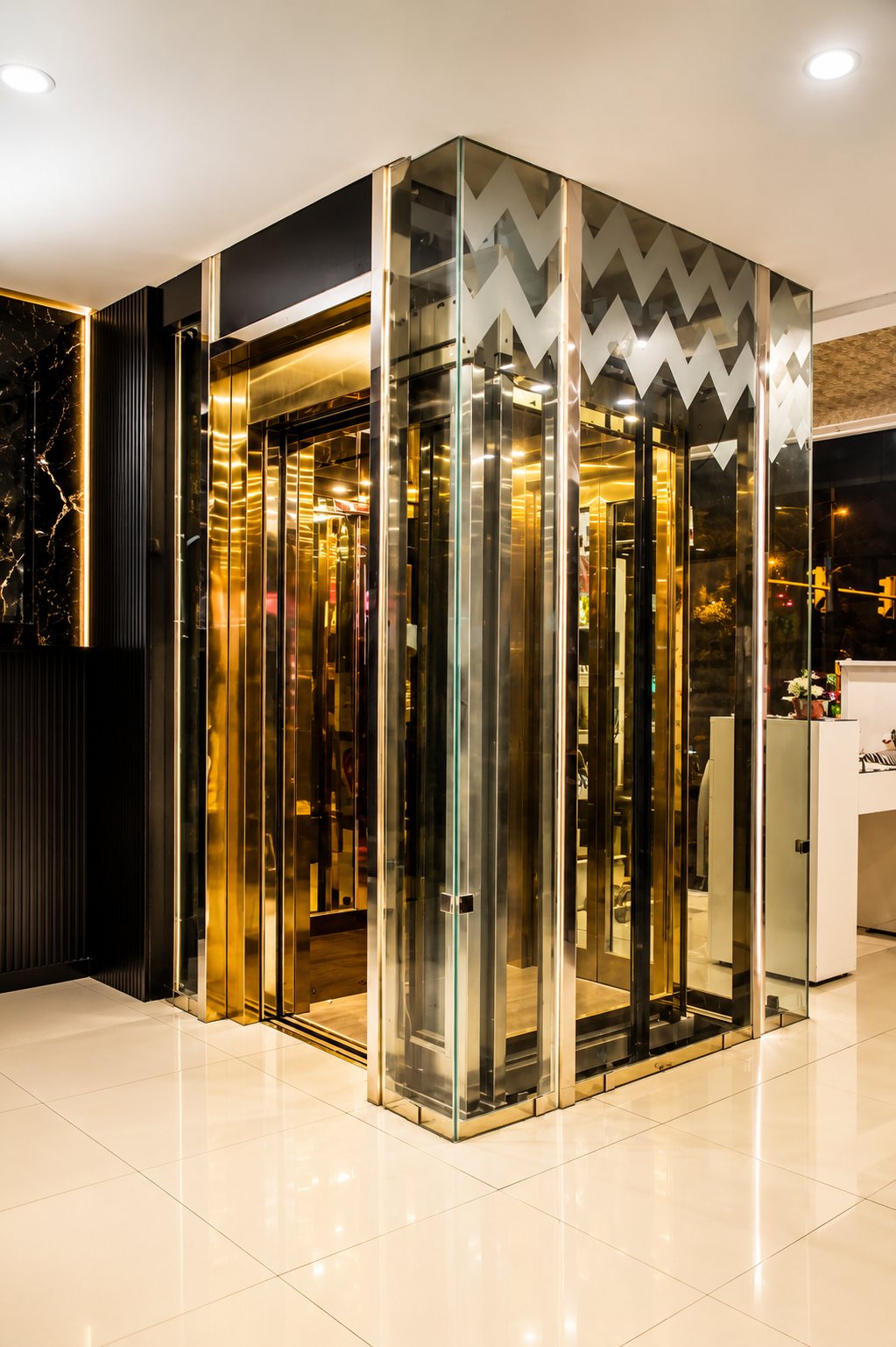 A Span passenger elevator with a mirror-gold hairline cabin inside a toughened structural-glass shaft with gold portal frames