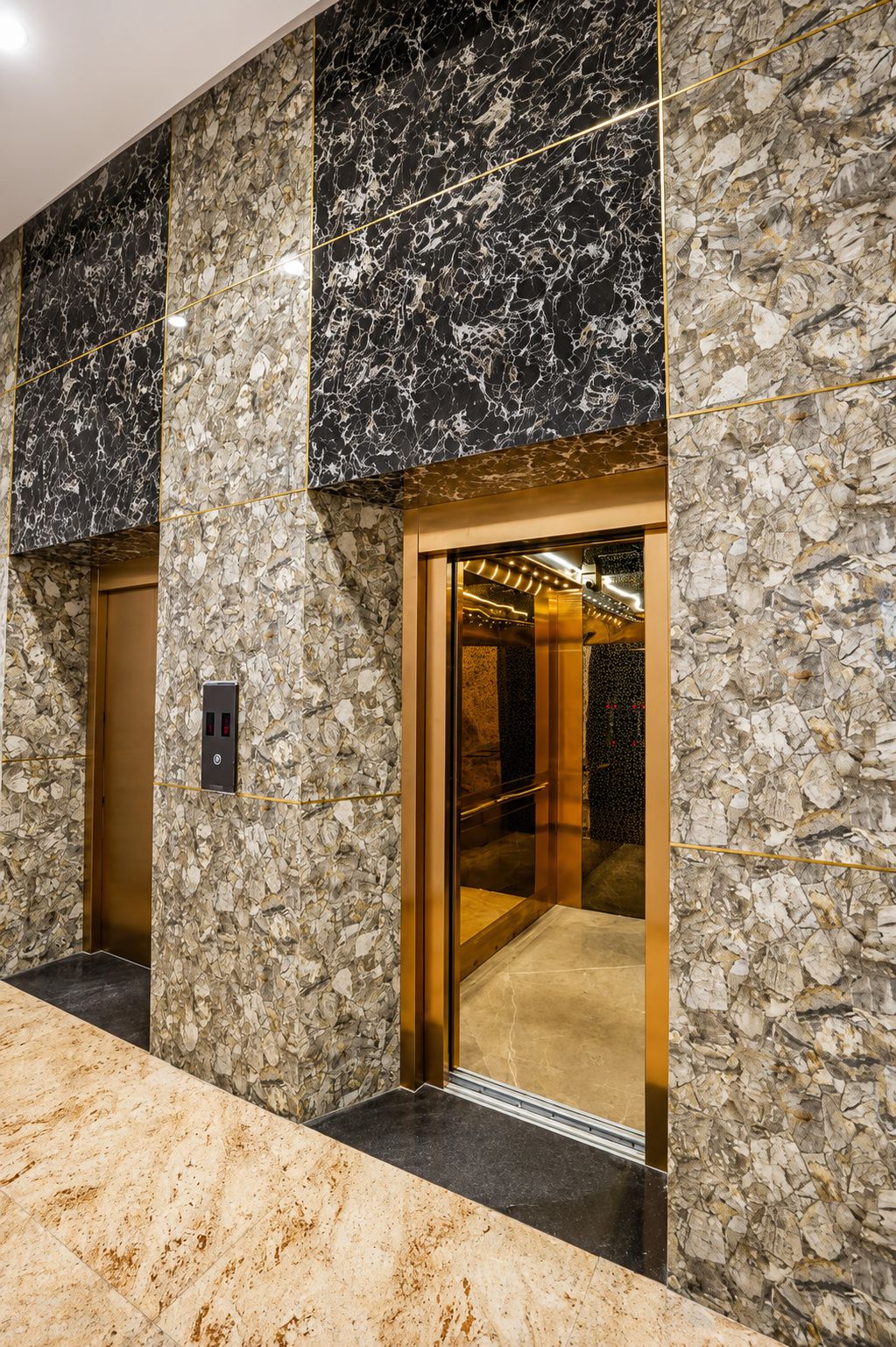 A Span passenger elevator with a bronze-gold mirror, centre-opening cabin in a commercial twin-lift bank with agate stone cladding and brass inlay